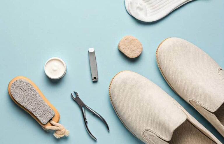 Et par hvide kanvas slip-on sko, en pimpsten, en negleklipper, en neglebåndsaks, en skobørste, en krukke creme og en hvid indersål er arrangeret på en lyseblå baggrund.