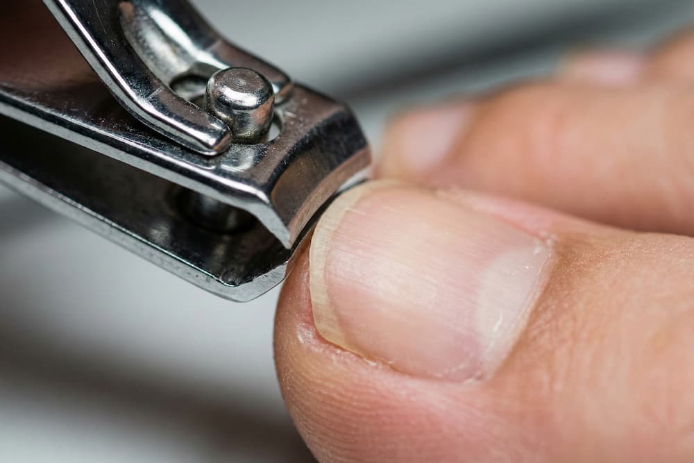 Et makro-nærbillede af en negleklipper i metal, der trimmer en tånegl lige over. Billedet demonstrerer den korrekte klippeteknik, der anbefales for at forebygge indgroede negle og opretholde sunde fødder.